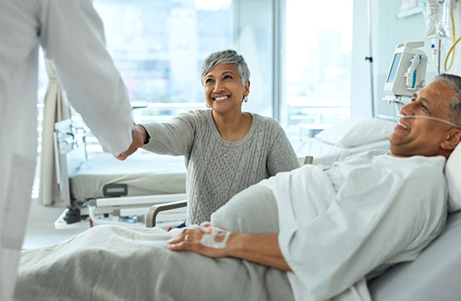 Man in hospital bed with caregiver next to him shaking health care provider’s hand.