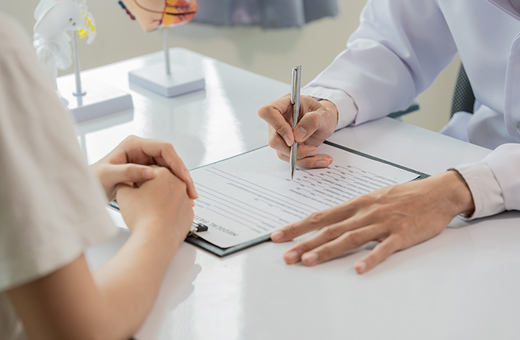 Plastic surgeon talking to patient at a desk with a clipboard.