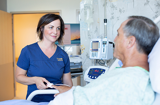 Nurse talking to male patient in hospital bed before robotic surgery.