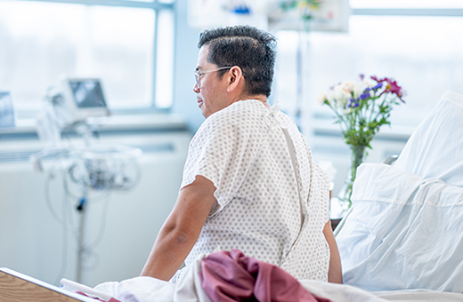 Man sitting on the edge of his hospital bed after surgery.