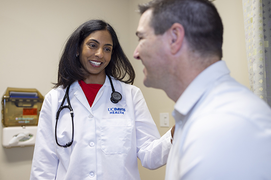 Female physician in a white coat with a stethoscope around her neck touching the shoulder of a male patient in an exam room