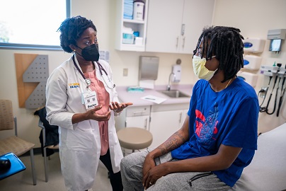 Younger male patient sitting on a clinic room table talking to a female health care provider