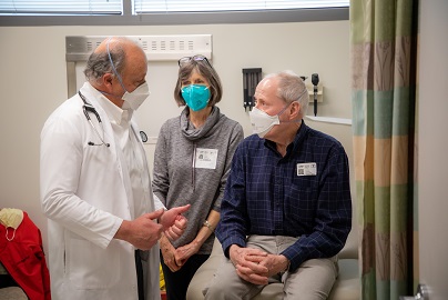 Male doctor talking to older male patient who is sitting alongside his wife in a clinic