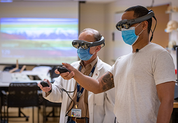 Michael Edwards and neurology resident Edwin Kulubya use mixed reality goggles. 