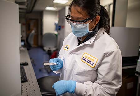 Woman in a white lab coat holds a plate for a mass spectrometer