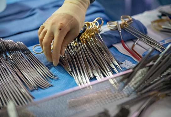 Hand with gloves on reaching for surgical scissors