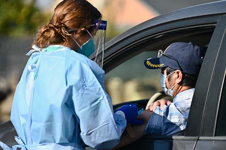 Students in PPE clothes giving shot to man in a car