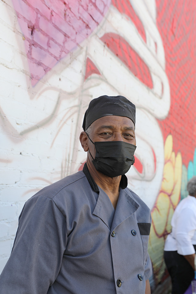 Chef Booker T. wears mask and stands in front of colorful painted graffiti wall