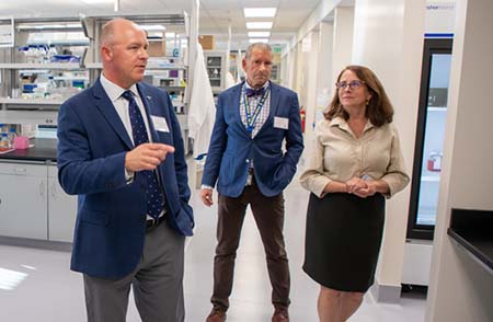 Two men and a woman walk through a laboratory