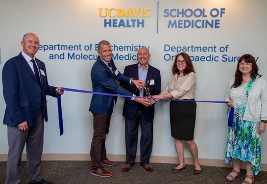 Five people standing and cutting a blue ribbon