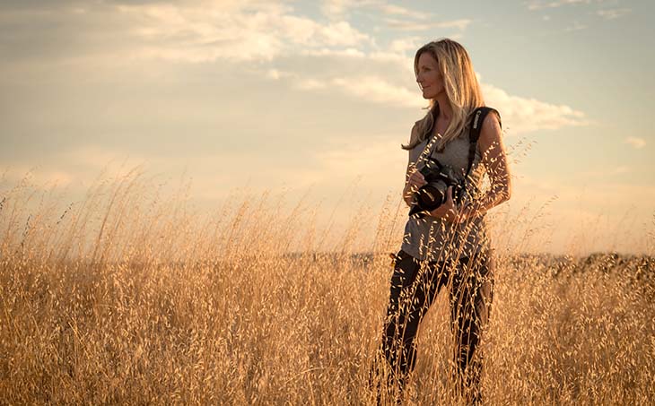 Jackie Anderson holding a camera while standing in a field and looking out at the horizon