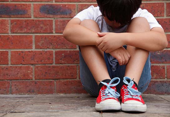 Child with red shoes sitting with head between legs