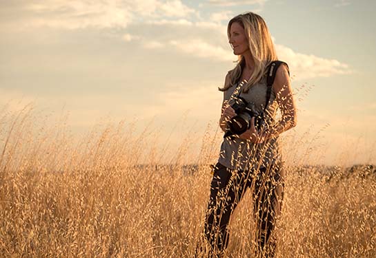 Jackie Anderson holding a camera while standing in a field and looking out at the horizon