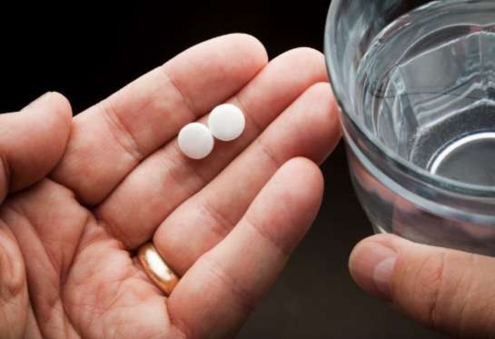 Hand holding two pills and glass of water