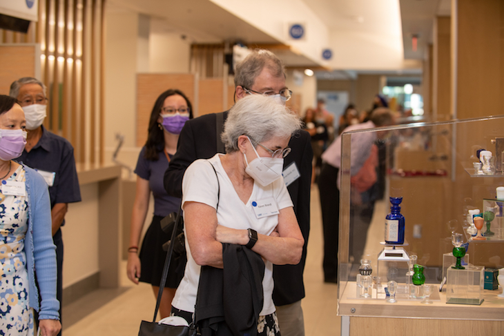 A woman wearing a mask looks at colorful objects displayed in a glass case