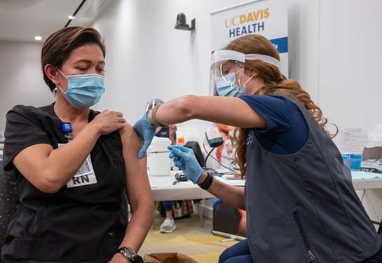 Woman wearing scrubs with sleeve rolled up and receiving injection in arm