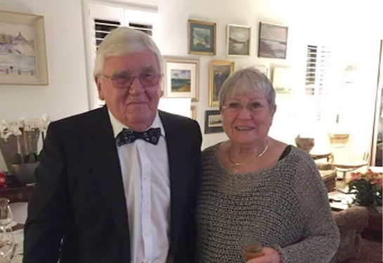 Hugo Bogren, wearing a tuxedo, smiles while standing next to his wife, Gunilla, who wears a fancy dress