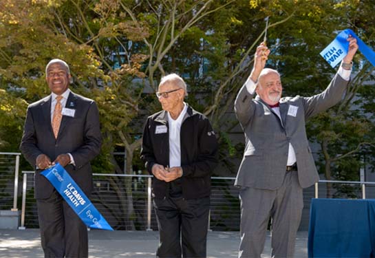 Three men are outside and holding pieces of blue ribbon with Davis Health written in in gold lettering.