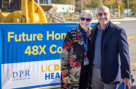 Blonde woman with short hair next to bald man standing in front of a yellow front loader