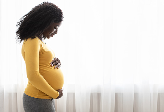  Beautiful pregnant black woman hugging her tummy at home