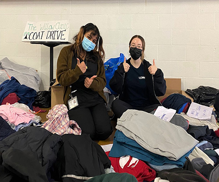 Two volunteers wearing scrubs sit among a pile of clothes that was given away at a previous Veterans Day Health Fair