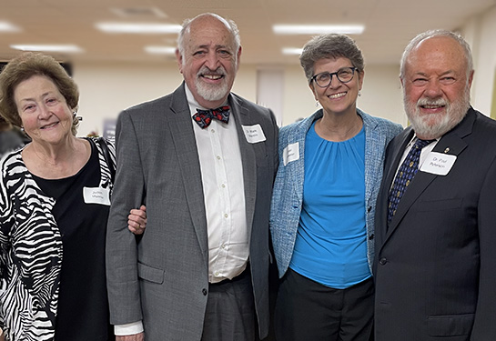 Four adults wearing business casual clothing, two women and two men, stand together as a group and smile for the camera.