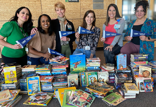 Six women standing behind table covered with books