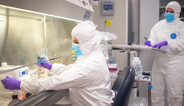 Two individuals full-geared in white protective coveralls working at UC Davis Good Manufacturing Practice Facility 