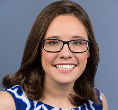 Woman with brown hair, glasses, and a white and blue blouse.