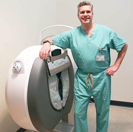 Man in scrubs leans against white circular machine