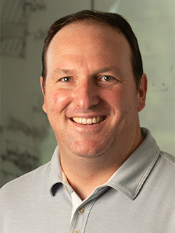 Headshot of a smiling man with receding brown hair wearing a grey polo shirt.