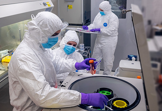 Three individuals in full protective gear working in the Good Manufacturing Practice facility