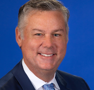 Man with graying hair, blue tie and navy blazer with blue background