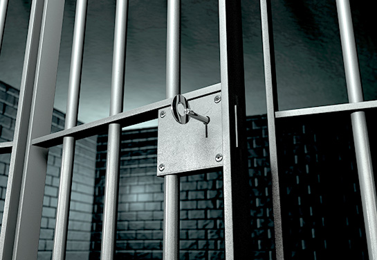 A jail cell with iron bars and a key in the locking mechanism with the door open.