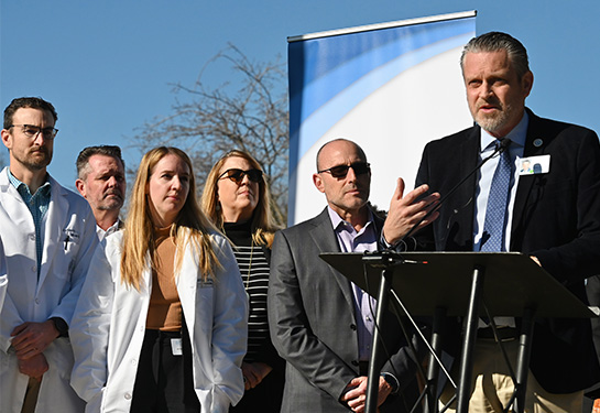 20 health professionals from UC Davis Health and WellSpace Health gather near a podium to hear remarks from WellSpace Health CEO Jonathan Porteus