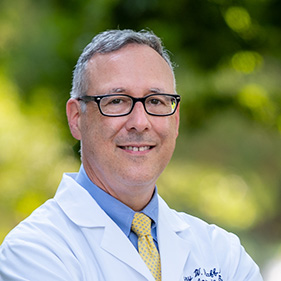 white male doctor in a white lab coat standing outside