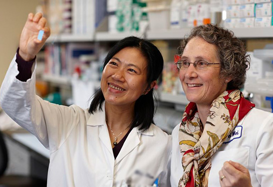 Woman holding a vile and another woman standing with her looking at vile