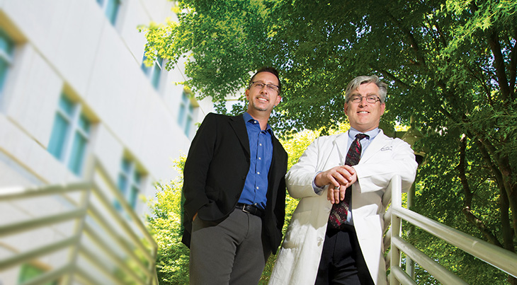 Two men standing side by side at the top of outdoor stairs. 