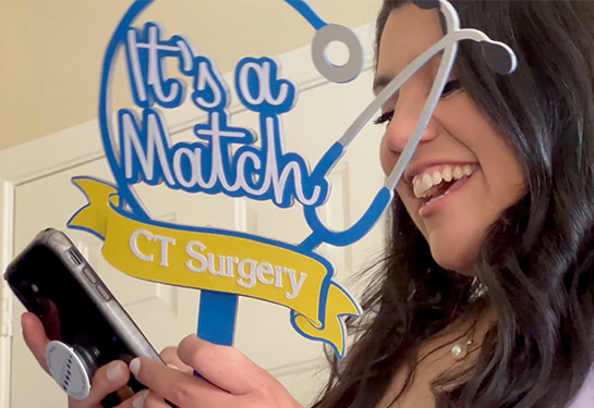 Medical student A young woman with long dark hair reads a congratulatory text on her cell phone while smiling widely. 