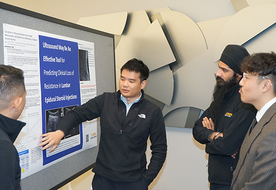 Student standing in front of poster explaining its meaning to person wearing white coat.