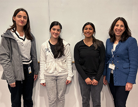 Three teenage girls on left, and their mentor Debbie A. Aizenberg, on right, pose in front of a white wall