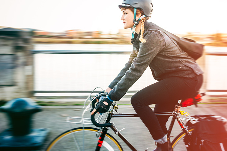 A smiling young woman commuting in an urban city environment on her street bicycle, waterproof panniers on her bike rack.