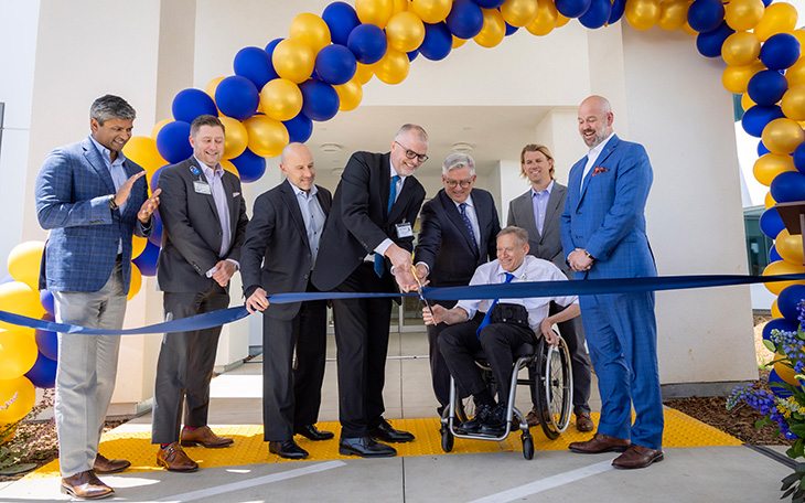 Seven men stand under a balloon arch at a ribbon cutting ceremony.