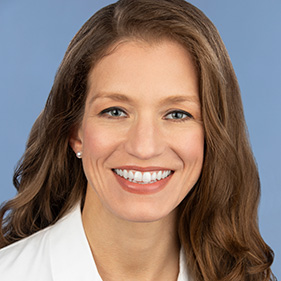 Dark-haired woman smiling and wearing a white coat