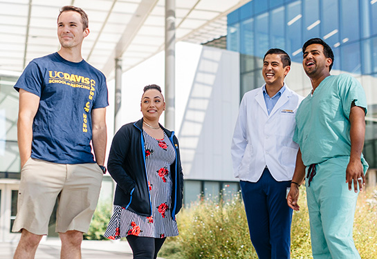 Four students from the School of Medicine and School of Nursing laugh and smile together in front of a glass-walled building