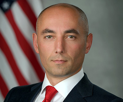 Man wearing a suit with an American flag behind him