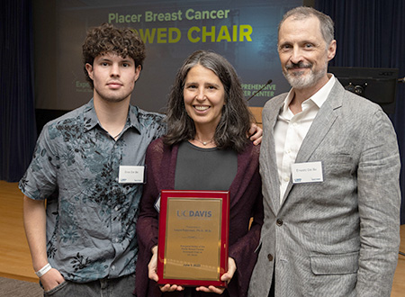 Woman standing between two men, younger man on left and older man on right.