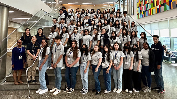 A group of about 60 high school students and four adults pose for a group picture standing on a wide stairwell