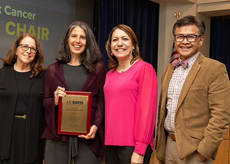 Four people standing with woman holding plaque. Three women on left and one man on right.