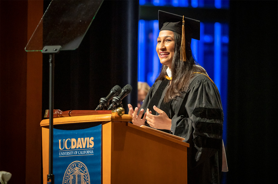 Selu Vargas speaks from podium wearing cap and gown